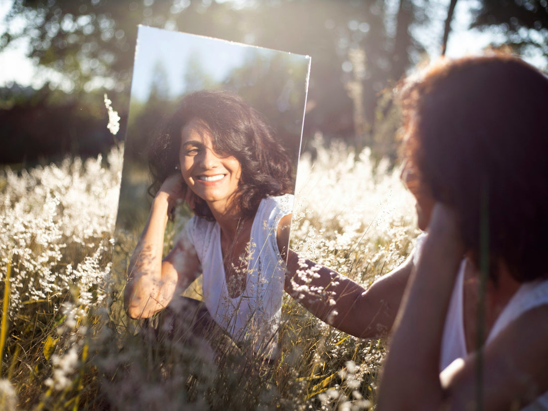 A woman looking into a mirror outdoors with a relaxed smile, symbolizing comfort during teeth whitening.