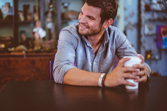 "Smiling man holding a coffee cup at a table, showcasing bright white teeth and a confident, relaxed demeanor."