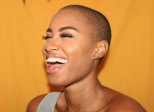 Confident woman with a radiant smile showing bright white teeth against a vibrant yellow background with the effect that Halo Pro Teeth Whitening Would present.