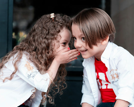 "Two children sharing a secret, with one whispering into the other's ear, both smiling brightly with healthy teeth."