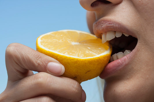 Close-up of a person biting into a lemon, symbolizing how acidic foods can harm tooth enamel and cause staining.
