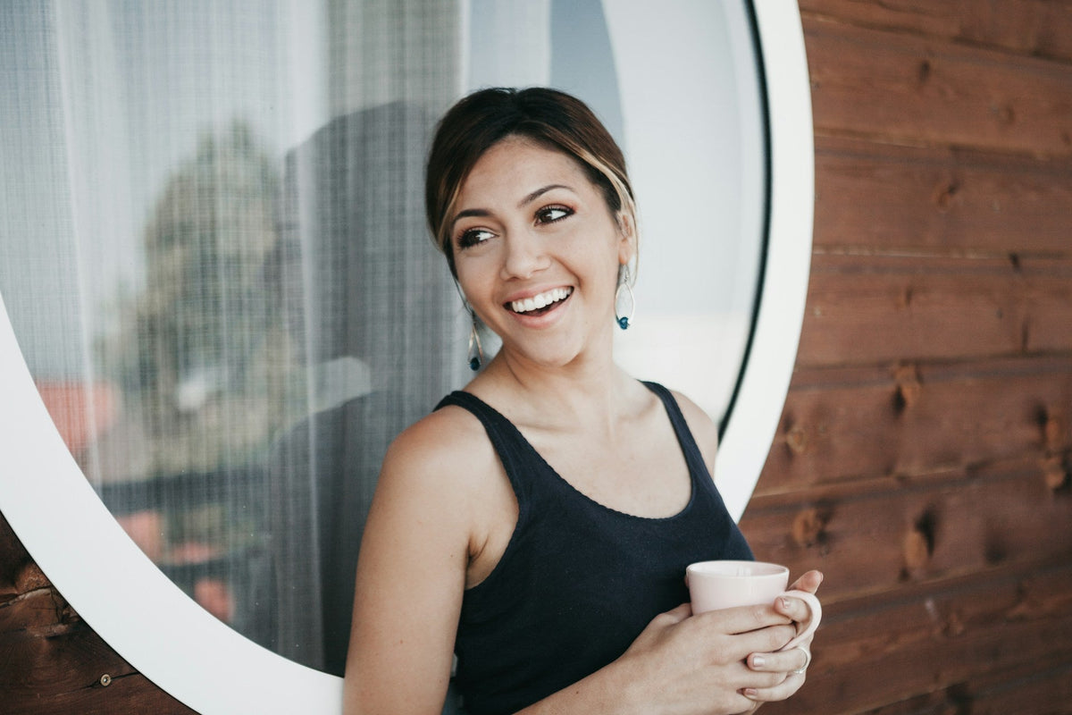 A woman holding a cup of coffee, smiling brightly, representing balance between indulgence and white teeth.