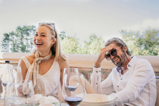 Smiling middle-aged couple enjoying a sunny outdoor lunch, symbolizing healthy teeth and gums through different life stages.
