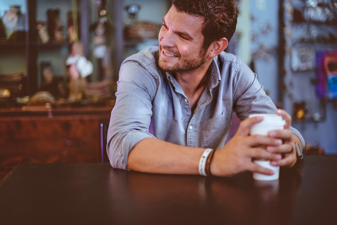 "Smiling man holding a coffee cup at a table, showcasing bright white teeth and a confident, relaxed demeanor."