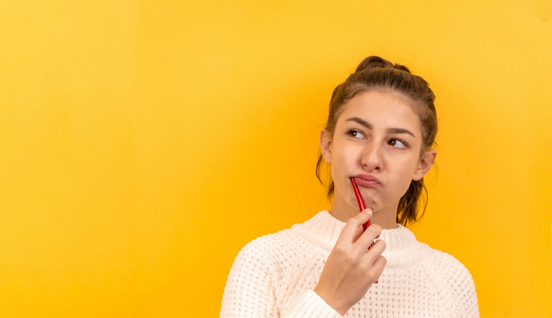 A young woman thoughtfully holding a red toothbrush against a bright yellow background, representing curiosity about dental care habits.