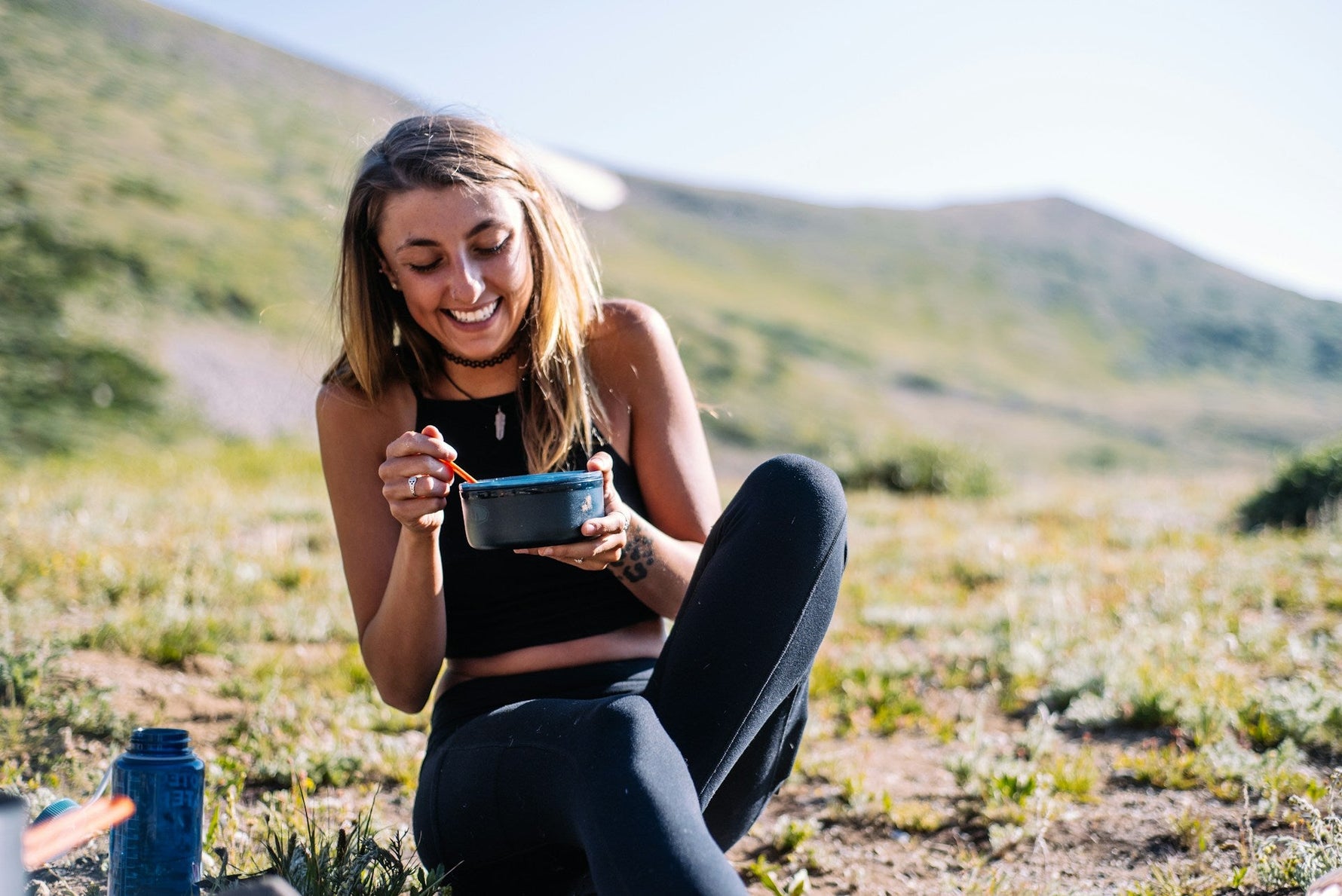 A smiling woman enjoying a meal outdoors in nature, symbolizing a healthy lifestyle and mindful eating habits for better oral health.