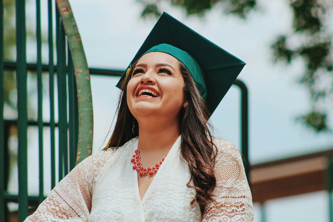"Young woman in a graduation cap smiling brightly with radiant white teeth, celebrating her achievement outdoors."