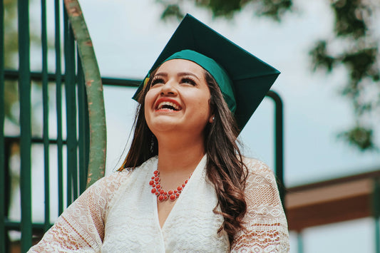 "Young woman in a graduation cap smiling brightly with radiant white teeth, celebrating her achievement outdoors."