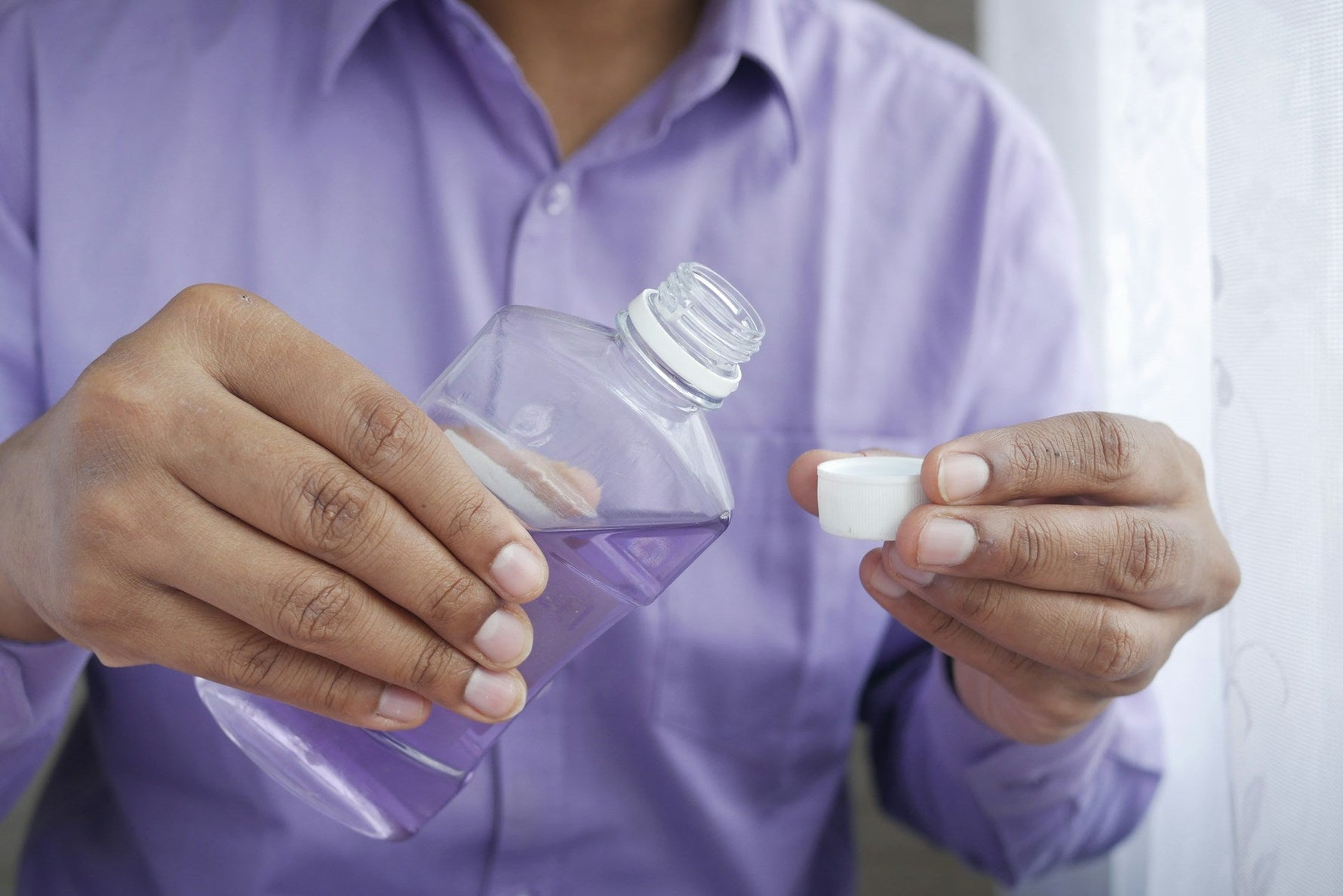 A person pouring mouthwash into a cap, preparing for oral rinsing, highlighting proper mouthwash usage.