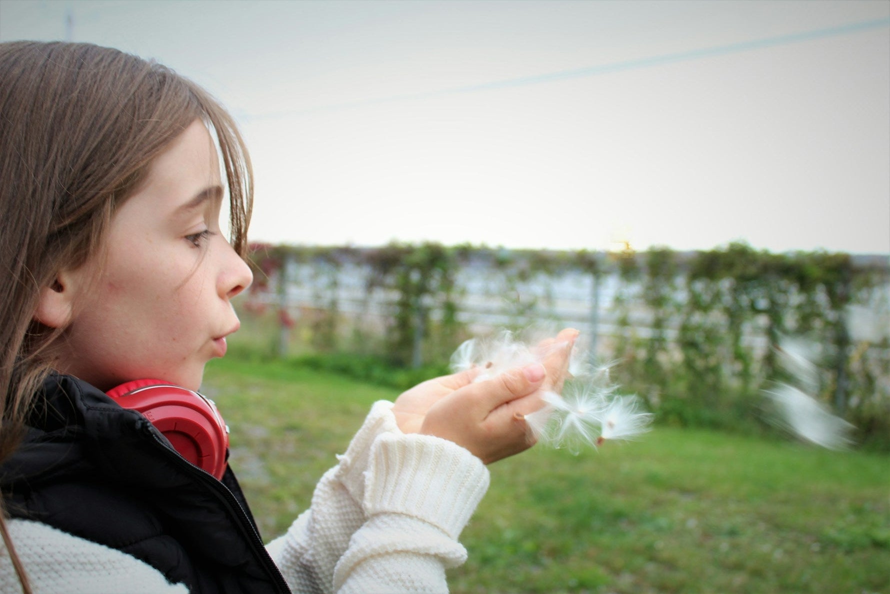 A young girl outdoors blowing dandelion seeds, symbolizing self-care and mindfulness.